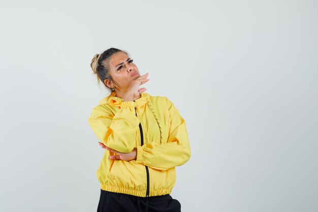 Vrouw die in sportkostuum kin bij de hand steunt en nadenkend, vooraanzicht kijkt.