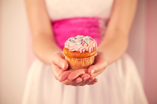 Vrouw die in witte kleding roze muffin houdt
