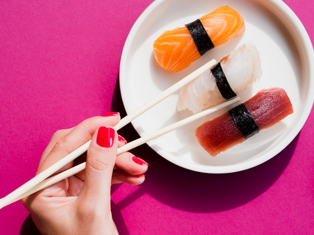 Vrouw die karbonadestokken gebruiken om sushi van plaat te plukken