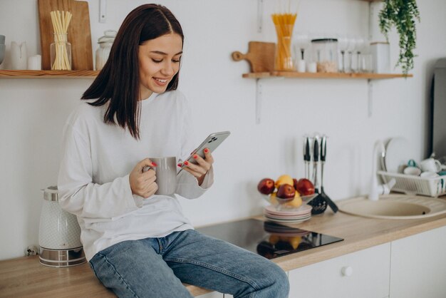 Vrouw die koffie drinkt en telefoon gebruikt in de keuken