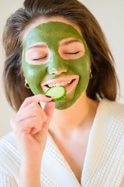 Vrouw die komkommerplak eet terwijl het hebben van een gezichtsmasker