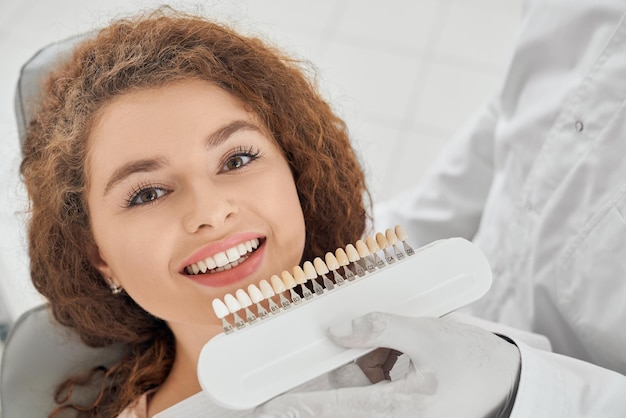 Vrouw die lacht terwijl mannelijke tandarts het kleurbereik van de tanden houdt
