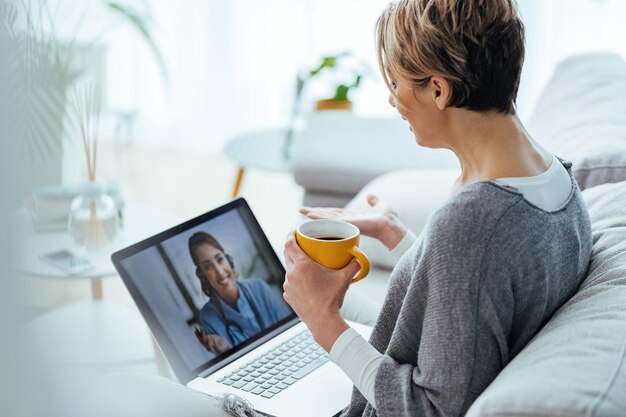 Vrouw die laptop gebruikt en videogesprek voert met haar arts terwijl ze thuis zit