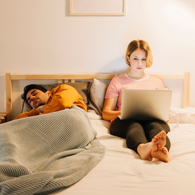 Gratis foto vrouw die laptop met behulp van dichtbij slaapman