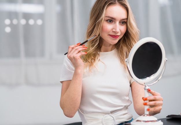 Vrouw die make-up doet terwijl het houden van spiegel