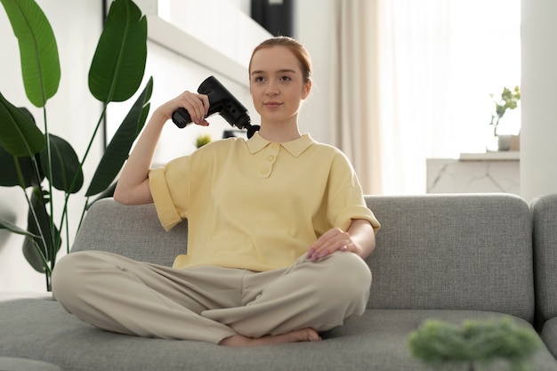 Vrouw die massagepistool gebruikt voor schouder volledig schot