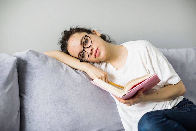 Vrouw die met boek en potlood camera bekijkt