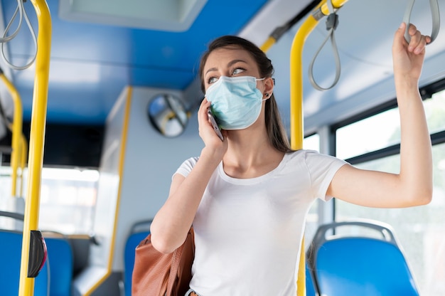 Vrouw die met de openbare bus reist en aan de telefoon praat terwijl ze een medisch masker draagt voor bescherming