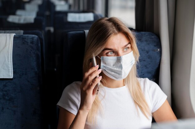 Vrouw die met de trein reist en aan de telefoon praat terwijl ze een medisch masker draagt