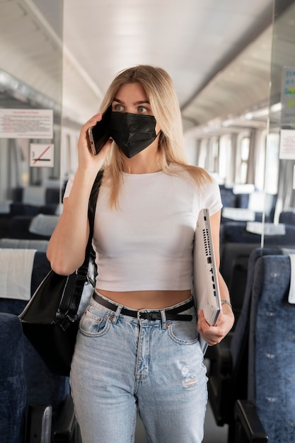 Vrouw die met de trein reist en aan de telefoon praat terwijl ze een medisch masker draagt