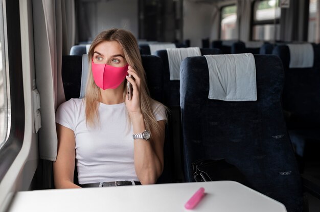 Vrouw die met de trein reist en aan de telefoon praat terwijl ze een medisch masker draagt