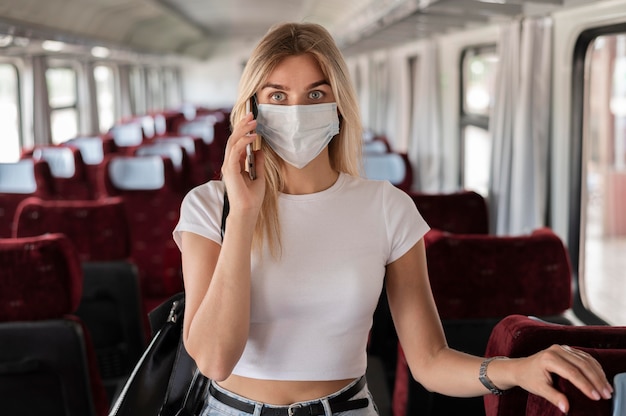 Vrouw die met de trein reist en aan de telefoon praat terwijl ze een medisch masker draagt