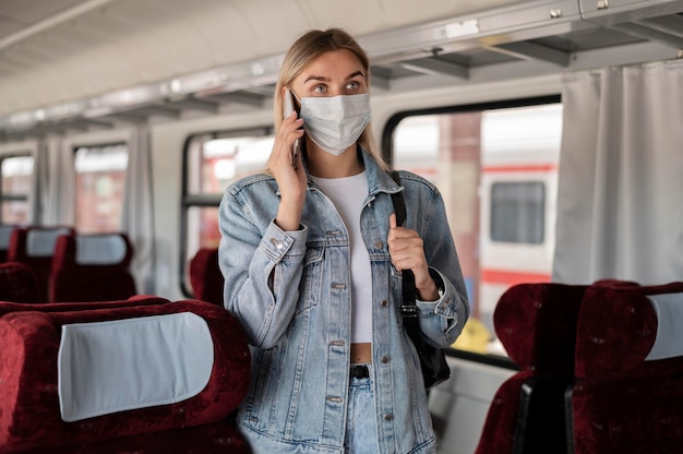 Vrouw die met de trein reist en aan de telefoon praat terwijl ze een medisch masker draagt