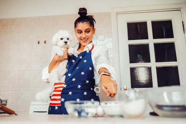 Vrouw die met de vinger in de keuken wijst terwijl ze de maltese hond vasthoudt