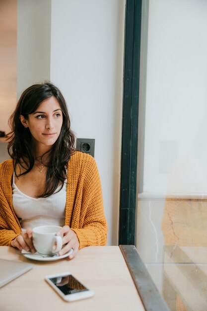 Vrouw die met drank uit venster kijkt