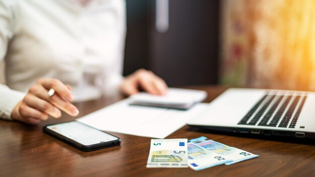 Vrouw die met financiën op de tafel werkt. Laptop, smartphone, geld, blocnote