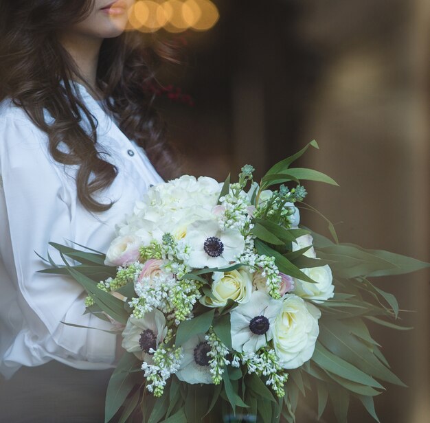 Vrouw die met krullende haren een wit boeket van bloemen houdt.