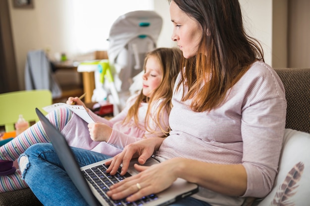 Vrouw die met laptop haar dochter het schrijven nota's bekijkt