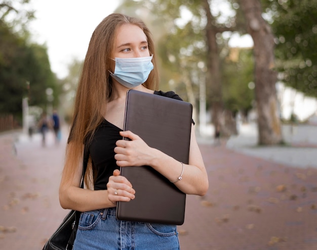 Vrouw die met medisch masker laptop buiten houdt