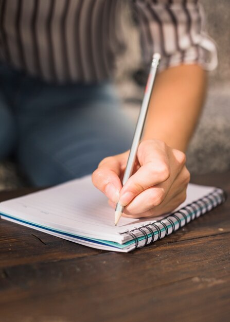 Vrouw die met potlood op spiraalvormig notitieboekje over de houten lijst schrijft