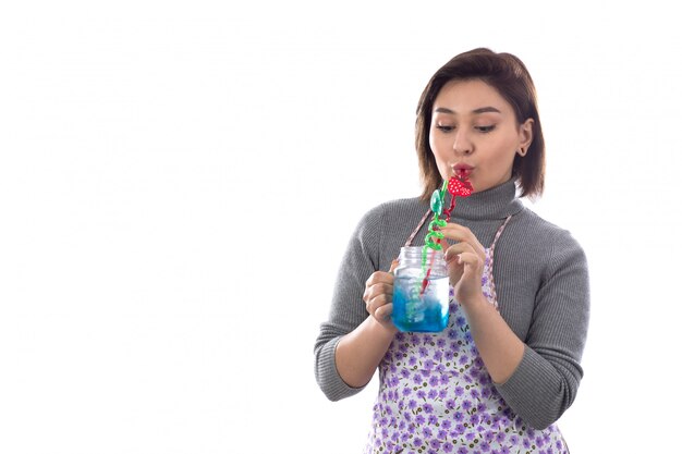 Vrouw die met purpere schort blauwe cocktail drinkt