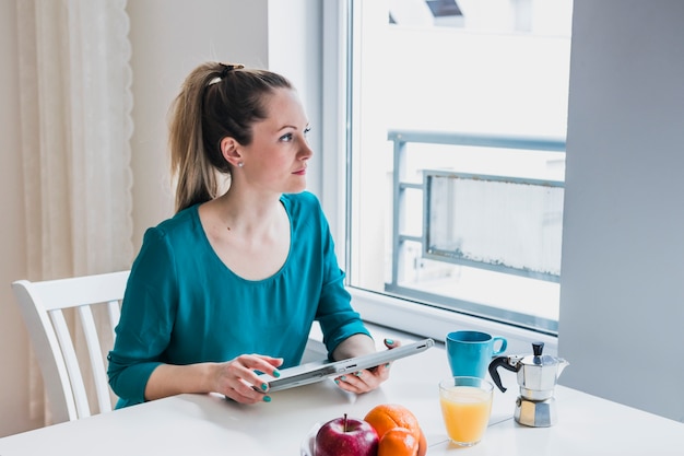 Vrouw die met tablet uit venster kijkt