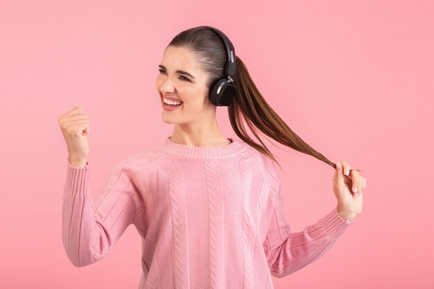 vrouw die naar muziek luistert in een draadloze koptelefoon met een roze trui die lacht, een vrolijke positieve stemming die zich voordeed op roze