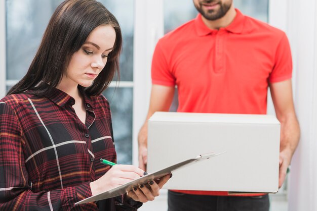 Vrouw die ontvangstbewijs dichtbij gewassenkoerier ondertekent