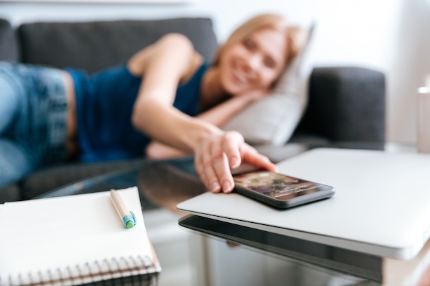 Vrouw die op bank ligt en mobiele telefoon van lijst neemt