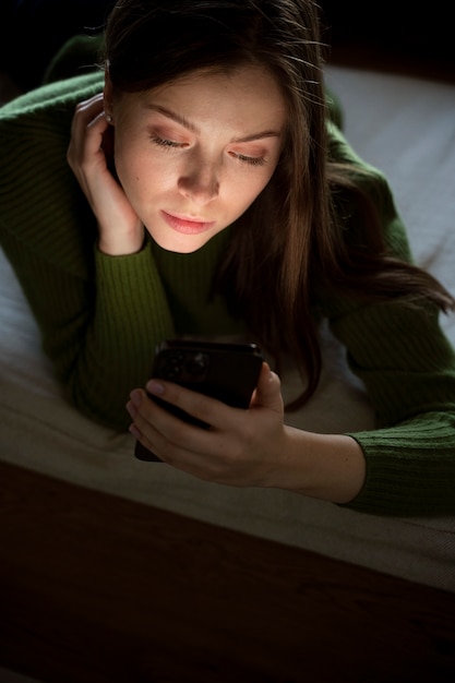 Vrouw die op bed ligt terwijl ze naar haar smartphone kijkt