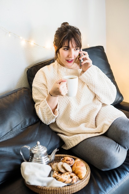 Vrouw die op cellphone spreekt die kop van koffie houdt