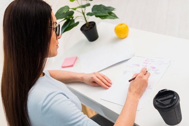 Vrouw die op documenten schrijft die bij lijst zitten