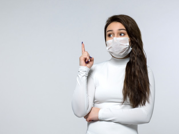 Vrouw die op haar vinger in witte kleding en wit medisch steriel beschermend masker wijst