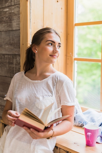 Vrouw die op het boek van de vensterholding in haar hand leunt