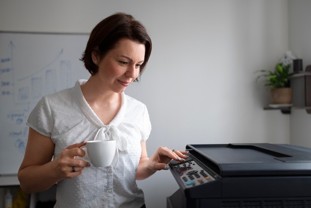 Gratis foto vrouw die op kantoor werkt en printer gebruikt