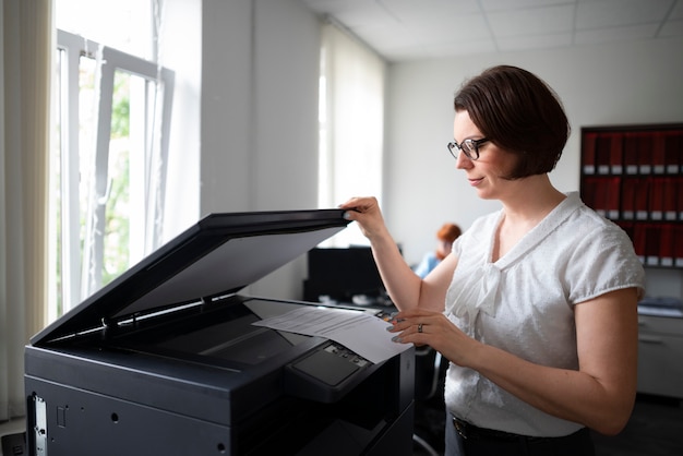 Gratis foto vrouw die op kantoor werkt en printer gebruikt