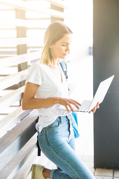 Gratis foto vrouw die op muur en doorbladerende laptop leunt