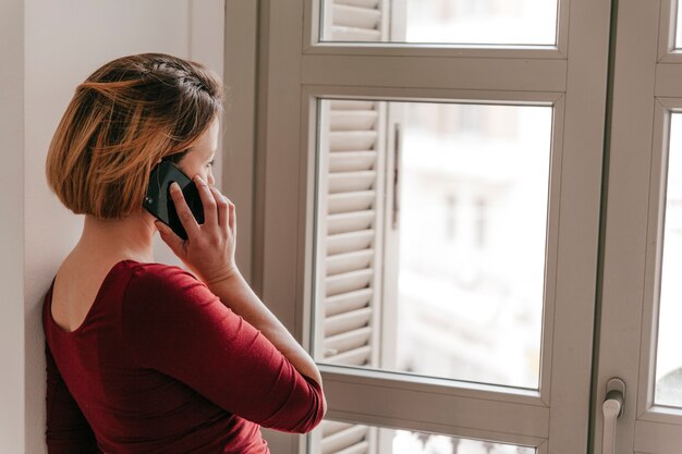 Vrouw die op smartphone dichtbij venster spreekt