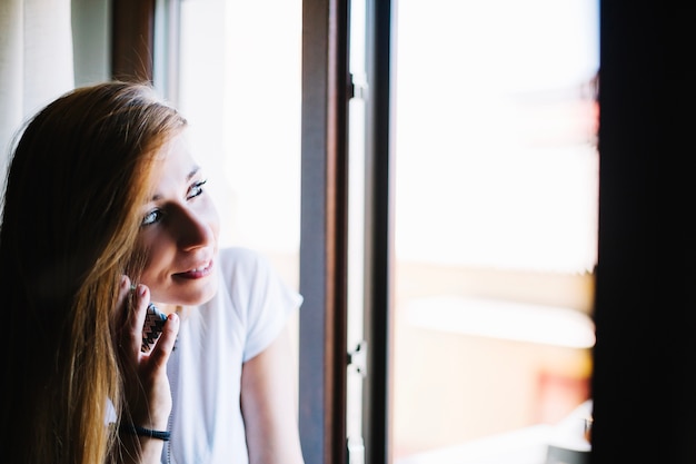 Vrouw die op telefoon dichtbij venster spreekt