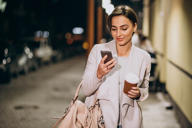 Vrouw die op telefoon en het drinken koffie buiten in de straat bij nacht spreken