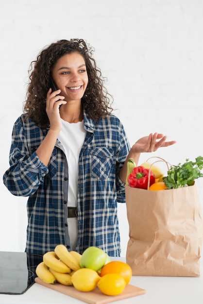 Vrouw die op telefoon spreekt en een groentenzak houdt