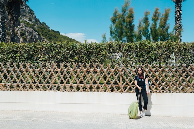 Vrouw die op tuinomheining leunt met in openlucht het houden van reizende kofferzak bij