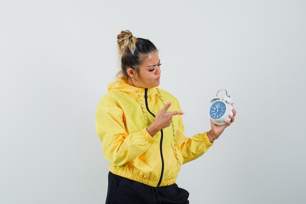 Vrouw die op wekker in sportkostuum richt en peinzend, vooraanzicht kijkt.