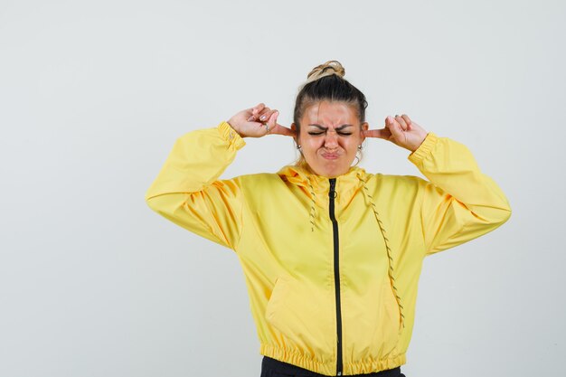 Vrouw die oren met vingers in sportpak verstopt en geïrriteerd, vooraanzicht kijkt.