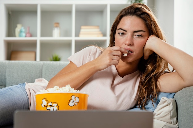 Vrouw die popcorn eet terwijl zij laptop bekijkt