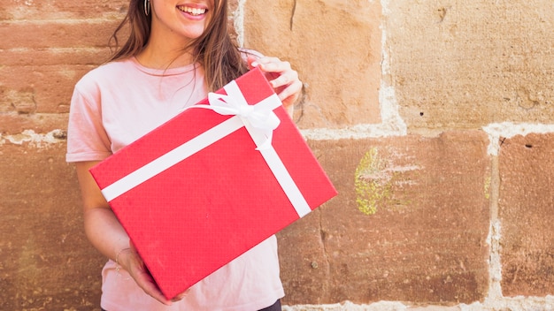 Vrouw die rode giftdoos houdt tegen doorstane muur