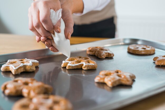 Vrouw die room toepassen op Kerstmis verse koekjes op dienblad