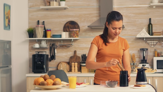 Vrouw die 's ochtends koffiebonen in de molen zet. Huisvrouw die thuis versgemalen koffie maakt in de keuken voor het ontbijt, drinken, koffie-espresso malen voordat ze naar het werk gaat