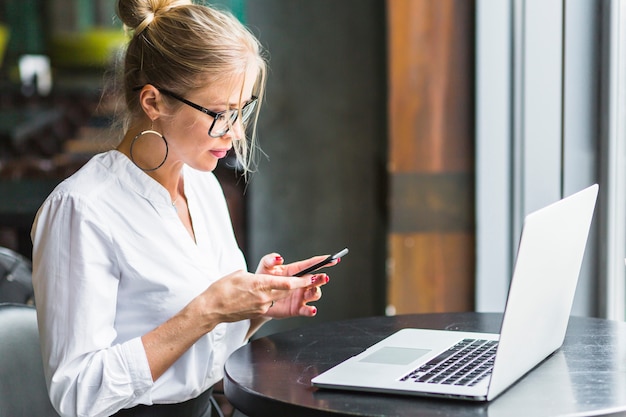 Vrouw die smartphone met laptop op bureau gebruikt