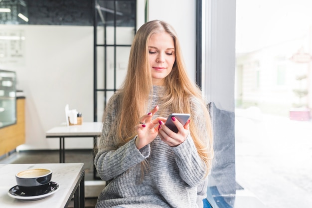 Vrouw die smartphonezitting bij koffielijst gebruiken